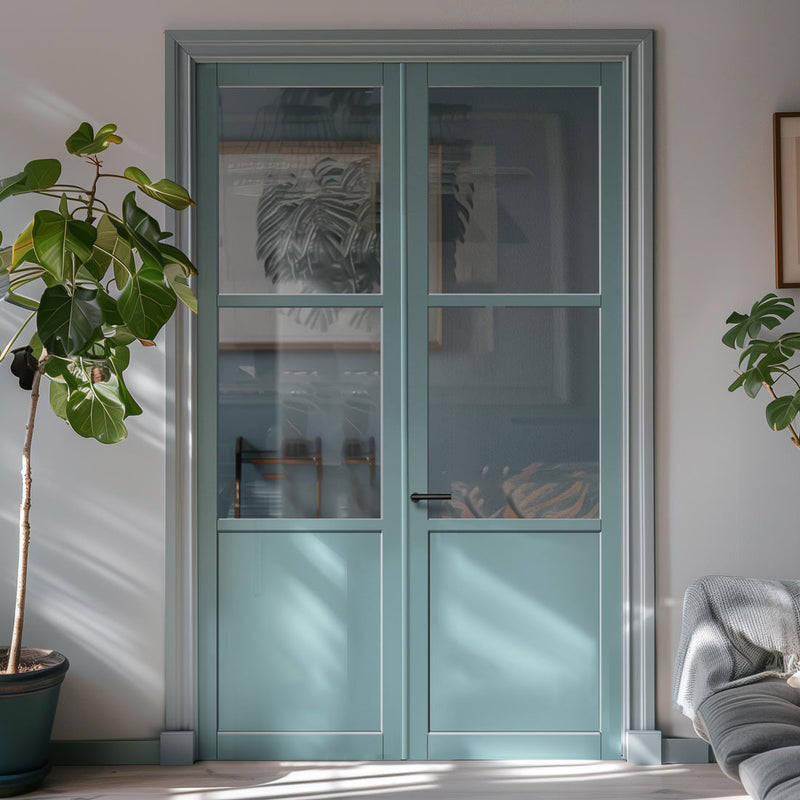 A pair of internal doors with clear glass panels, primed and painted in a sage sky color, installed in a room with a gray floor and walls, alongside a potted plant and a chair.