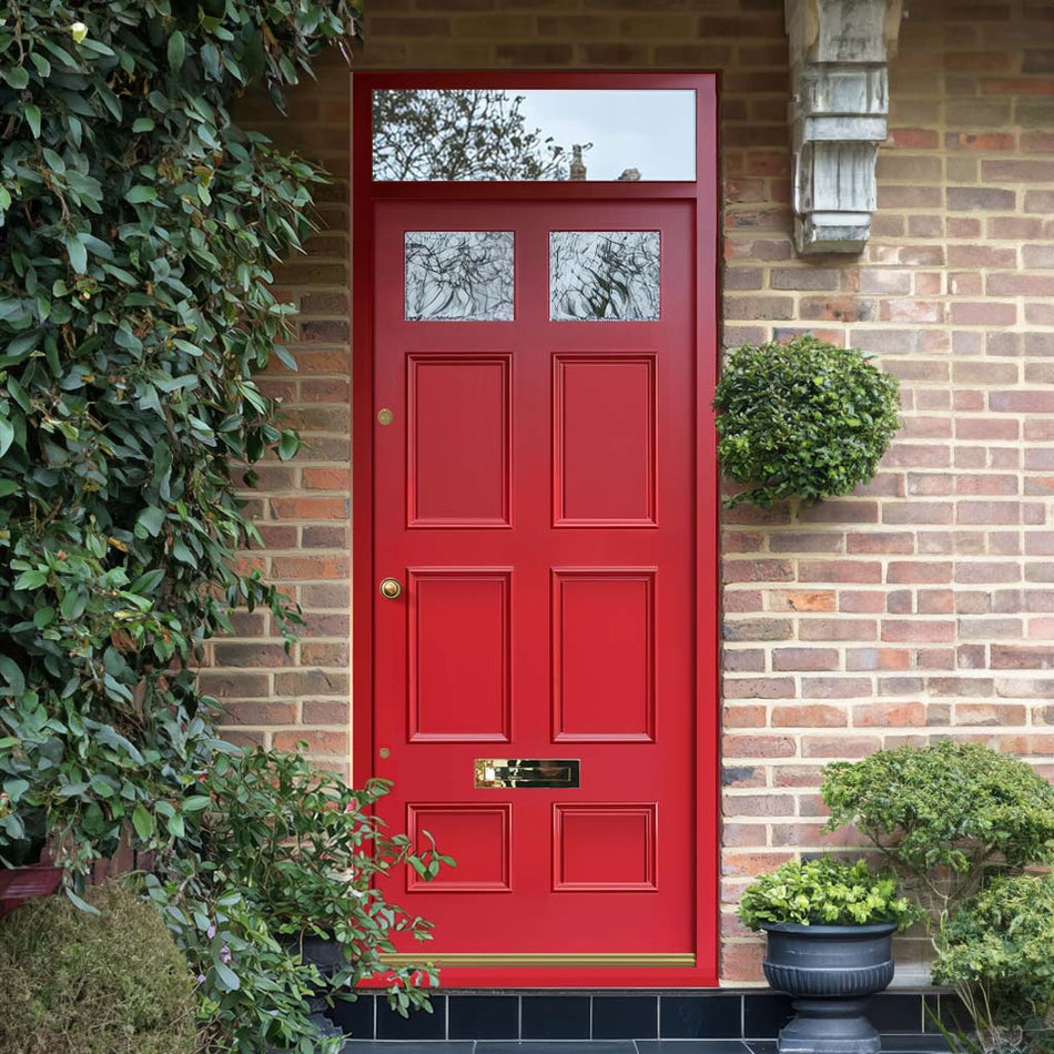 A red Victorian-style front door with a transom window, situated on a brick wall with a small bush in front and a larger bush to the side.
